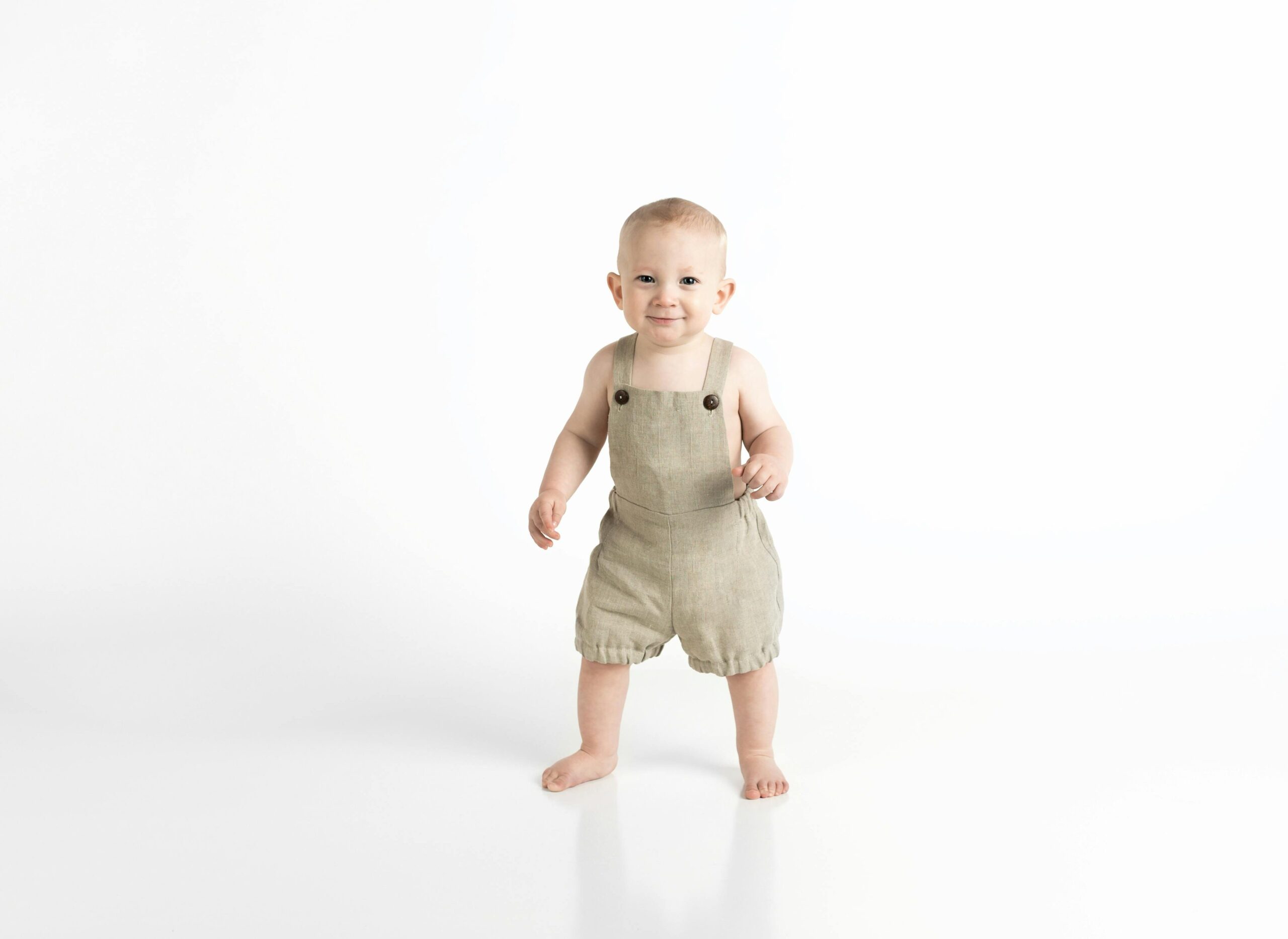 pexels photo 961198 961198 Adorable baby in beige overalls standing against a white background, showcasing innocence and joy.